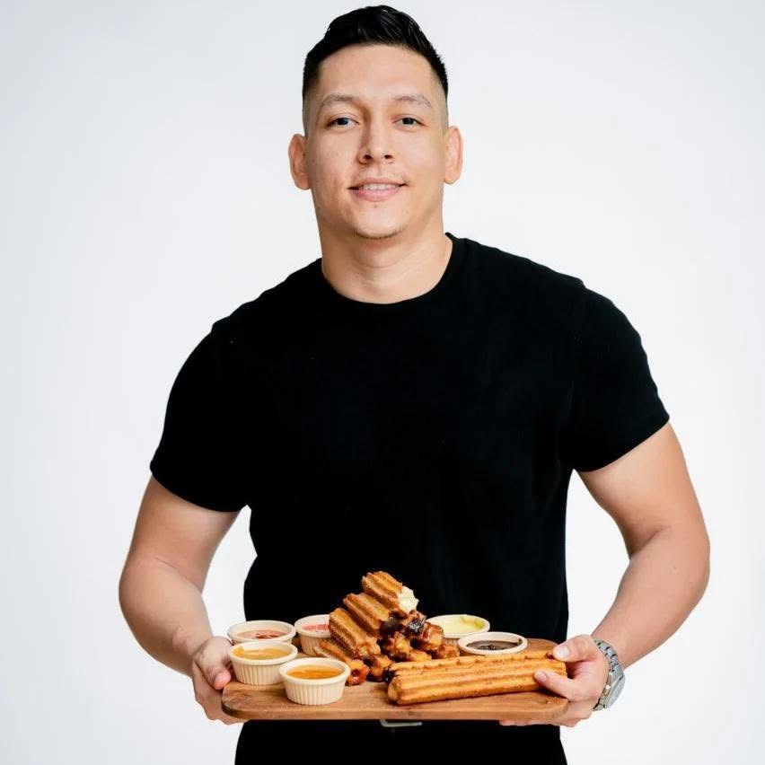 El fundador de Papi Churro sosteniendo una tabla de churros con salsas